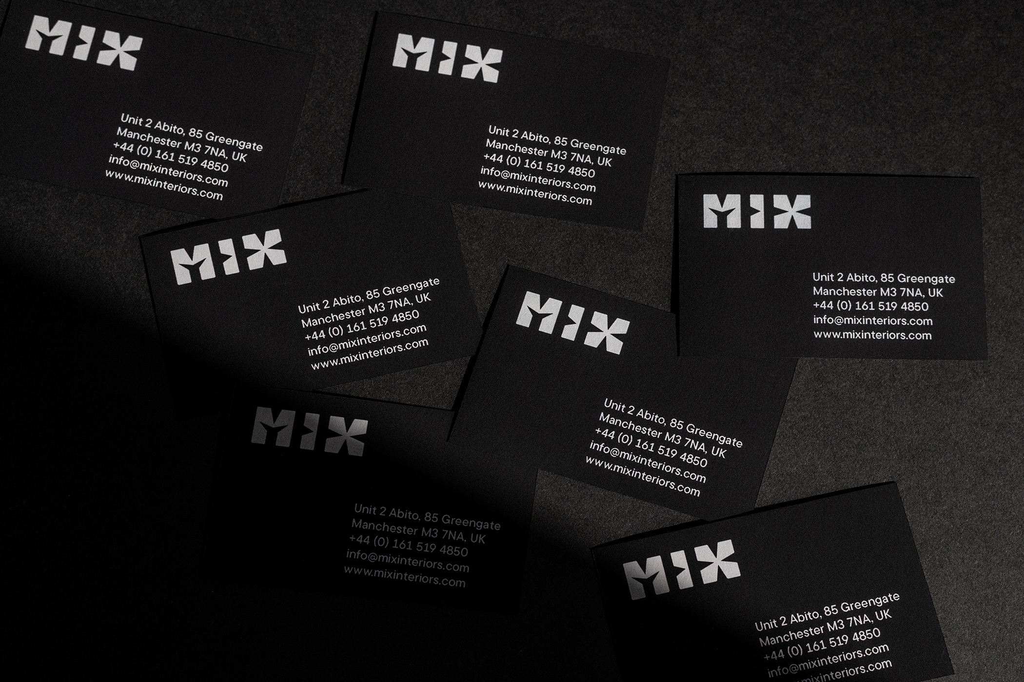 Black MIX business cards with the white logo scattered on a dark textured surface