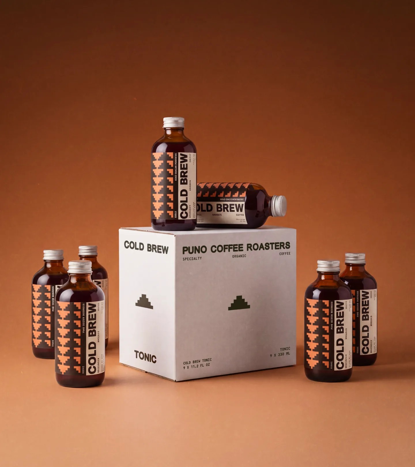 Five PUNO Coffee cold brew bottles with peach-and-black pyramid labels around a tonic box