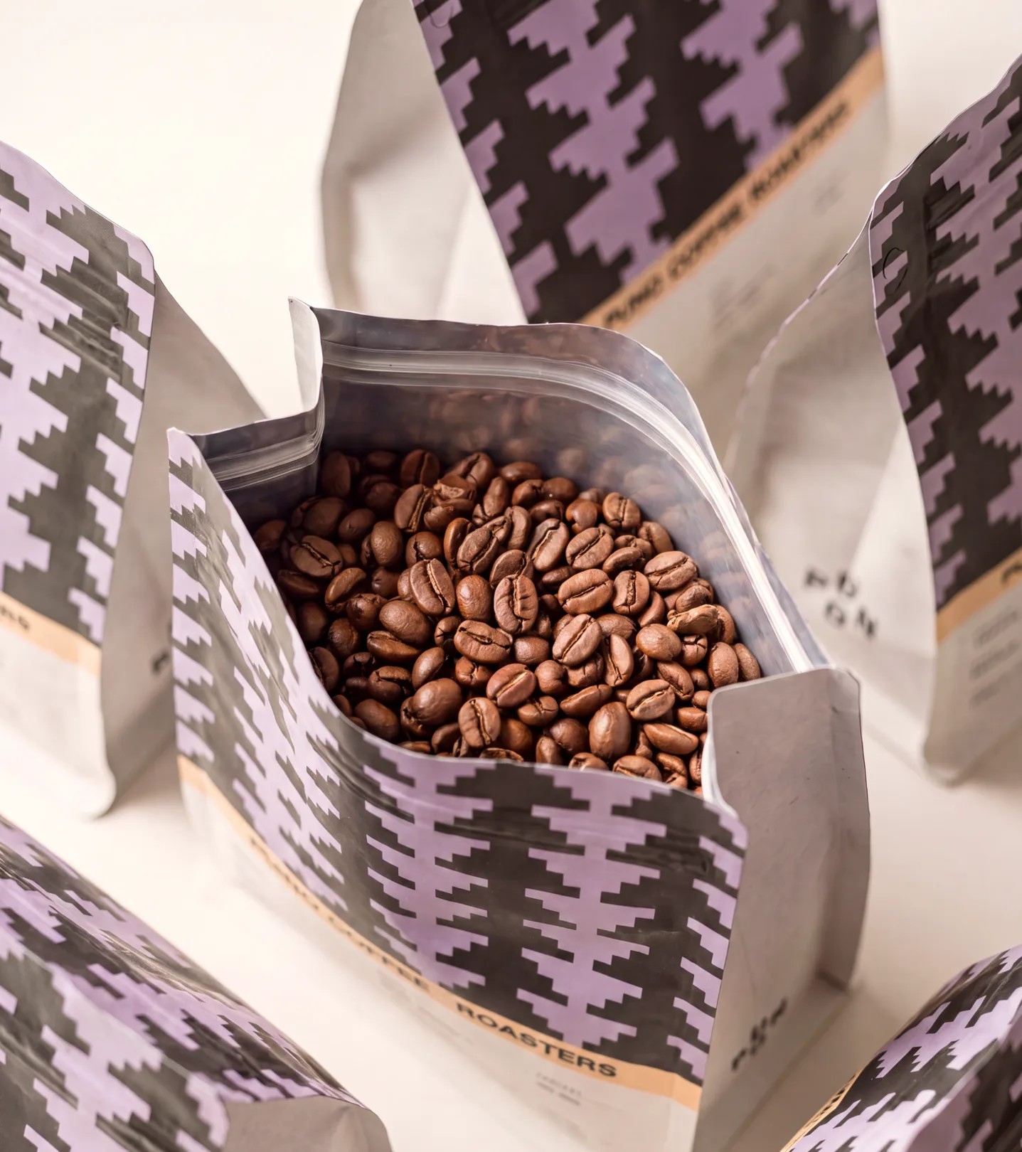 PUNO Coffee whole-bean bags with lavender-and-black stepped pyramid pattern, central bag opened showing whole beans