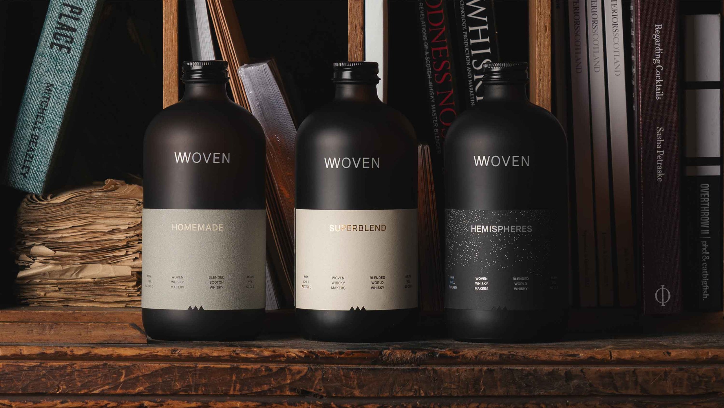Three frosted brown Woven whisky bottles on a bookshelf, Homemade, Superblend and Hemispheres labels visible.