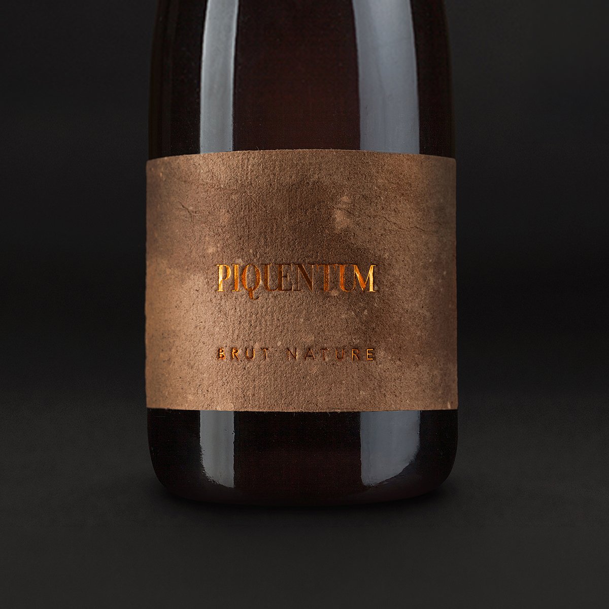 Piquentum Brut Nature bottle with its clean sediment-paper label: PIQUENTUM in gold serif capitals above letterspaced BRUT NATURE, dark background