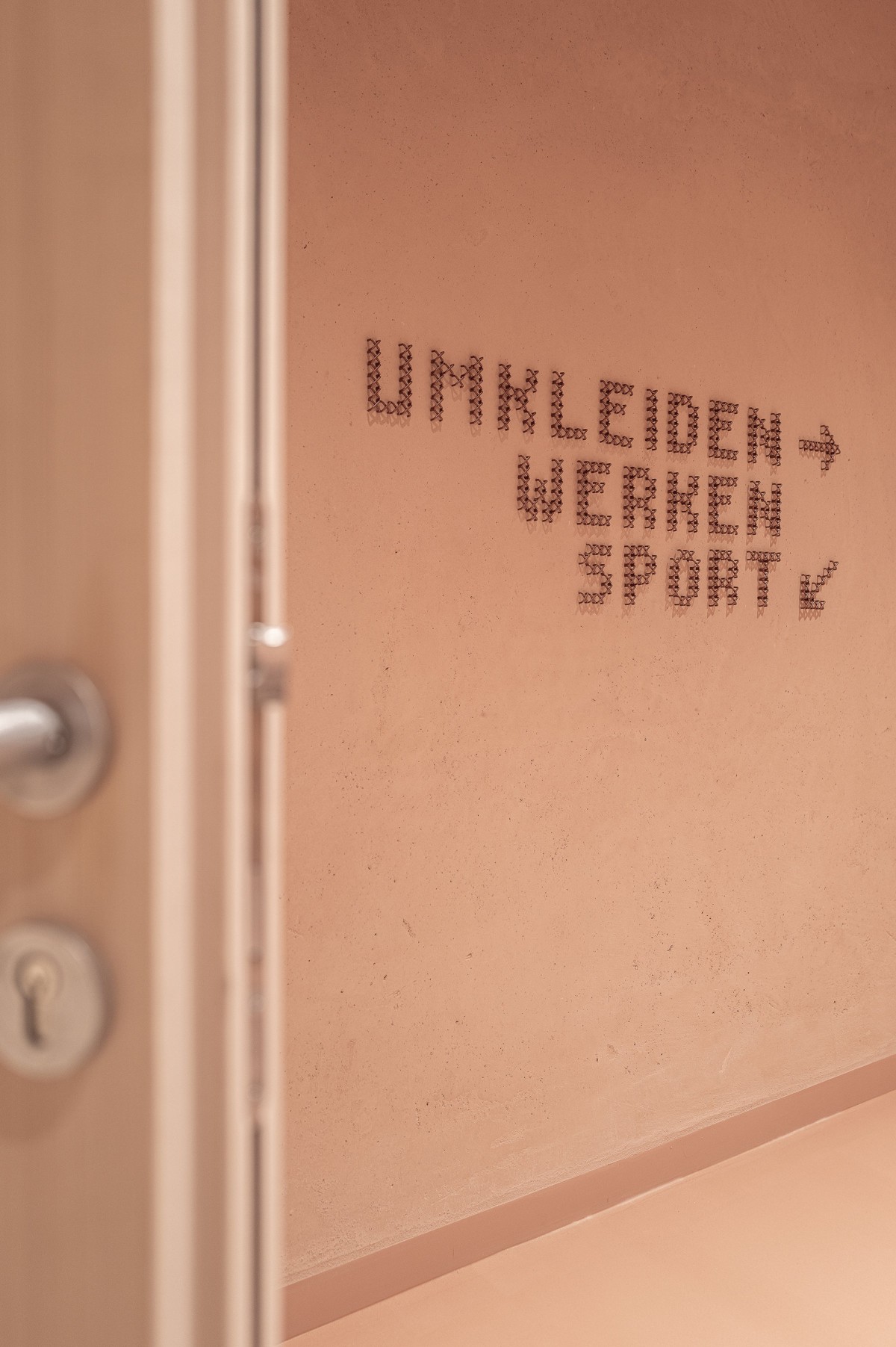 Macro detail of a copper cross-stitch arrow on warm plaster at Education Center Kössen