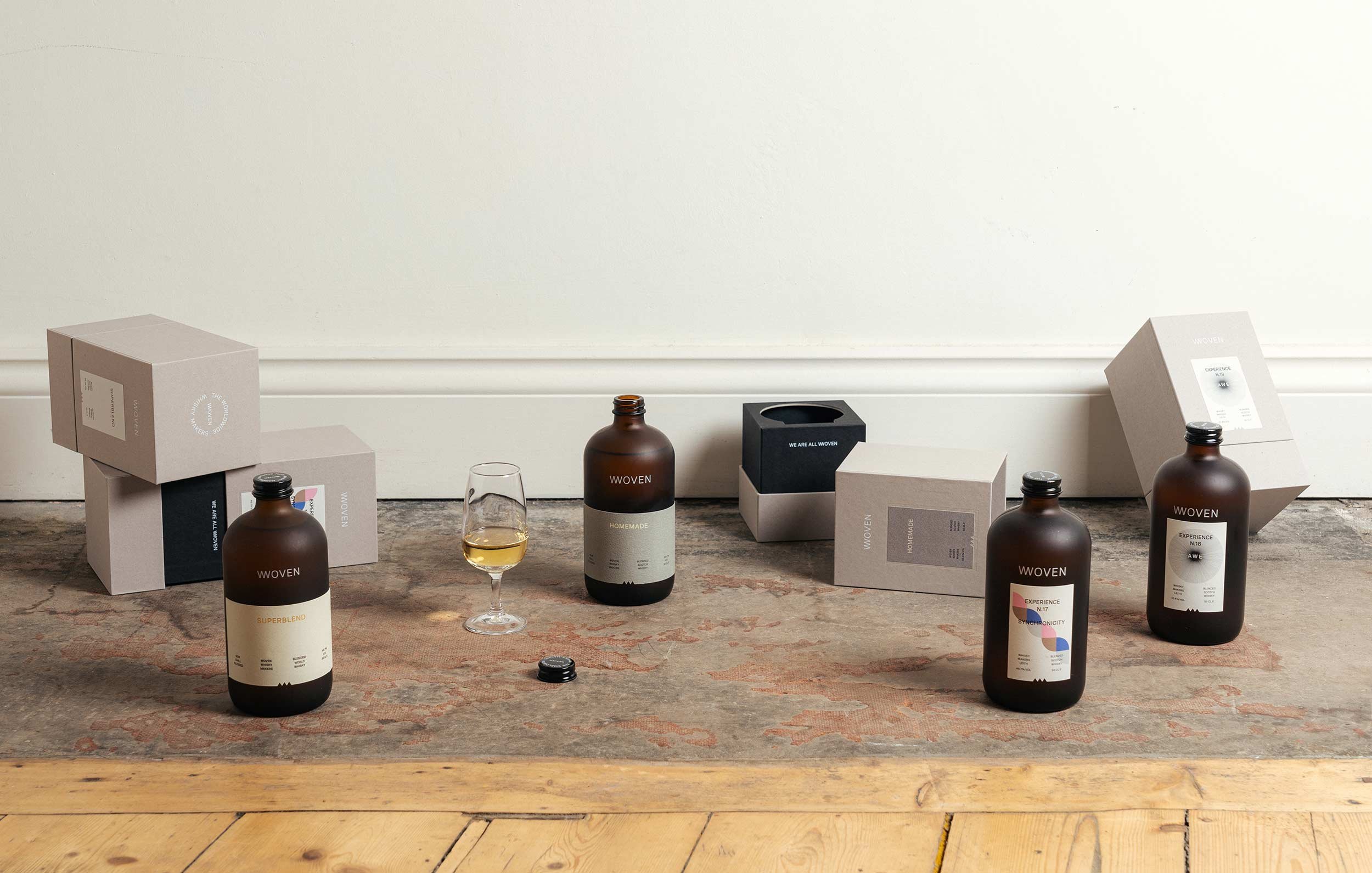 Full Woven range on a floor, core bottles, limited editions, grey boxes and a tasting glass.
