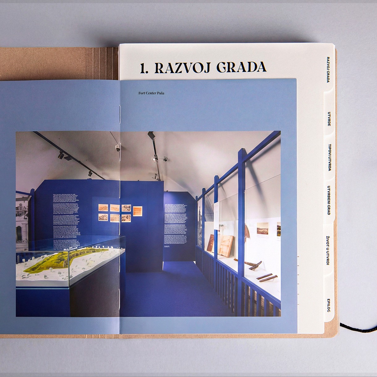 Spread pairing a tabbed chapter page with a full-page photograph of the Fort Center Pula exhibition installation.