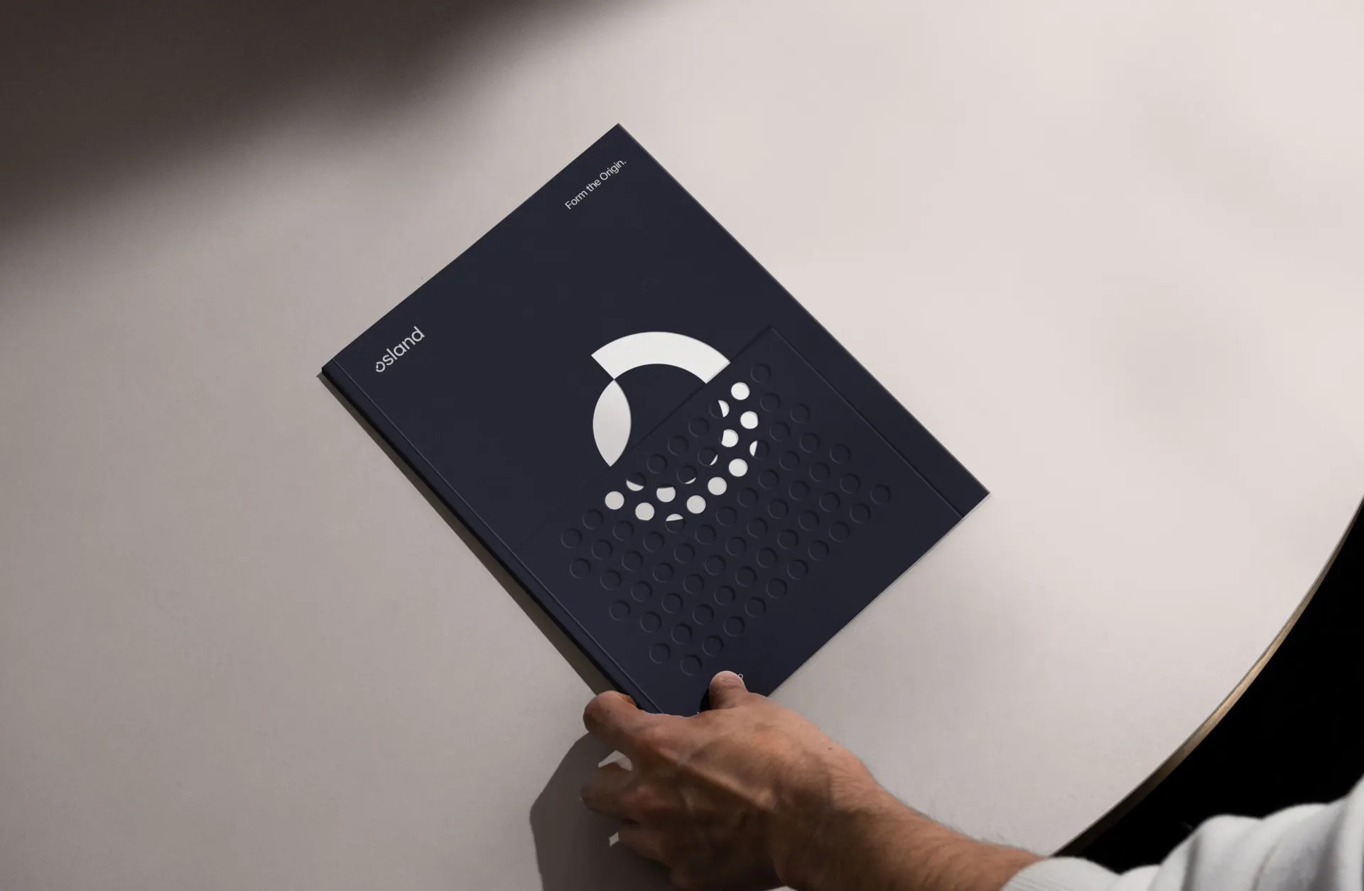 Dark blue Osland booklet with the white circular mark, held open to show the print finish
