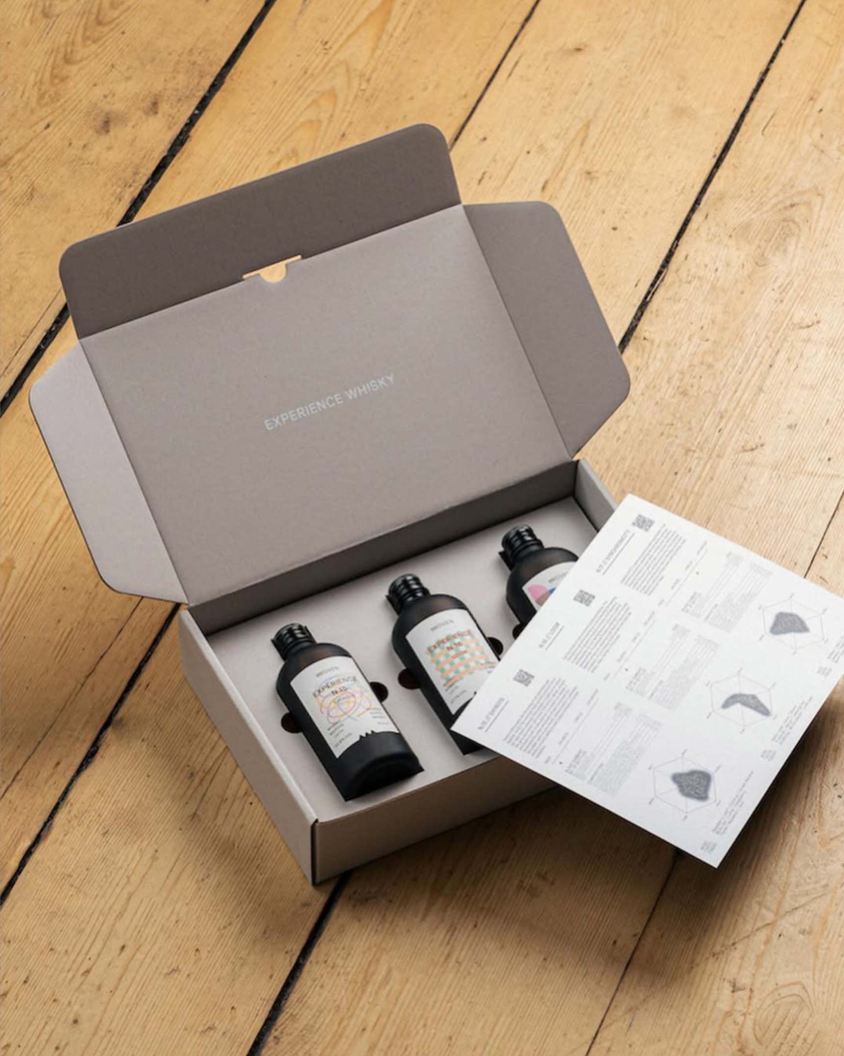 Open Woven gift box with three small bottles and a printed tasting leaflet showing flavor charts.