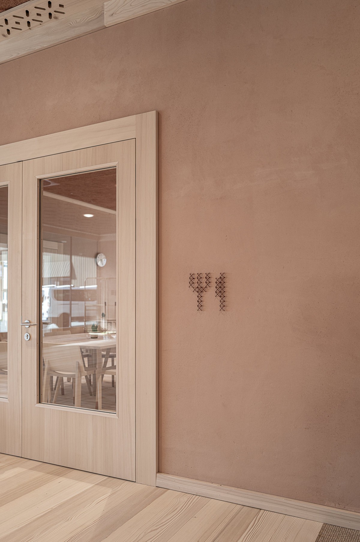 Glass doors with a small copper cross-stitch sign at Education Center Kössen