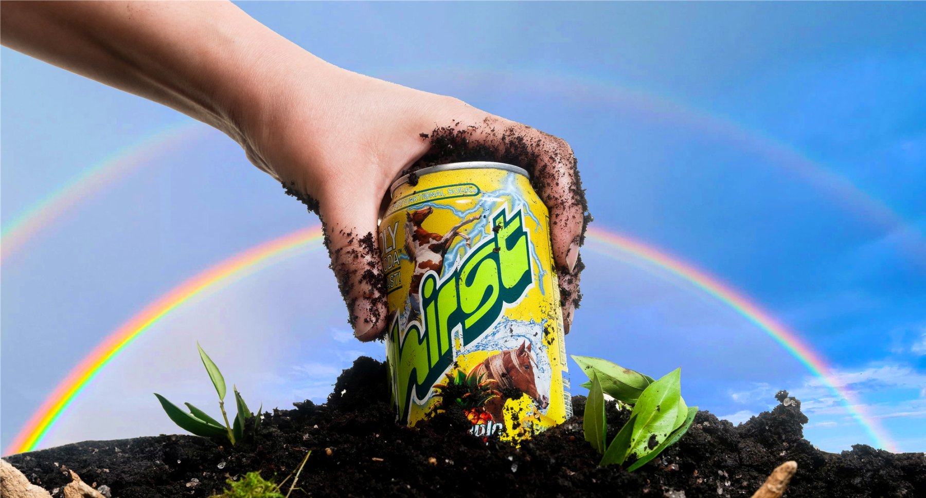Hand holding a Fhirst Pineapple Yuzuphoria can against soil and a rainbow