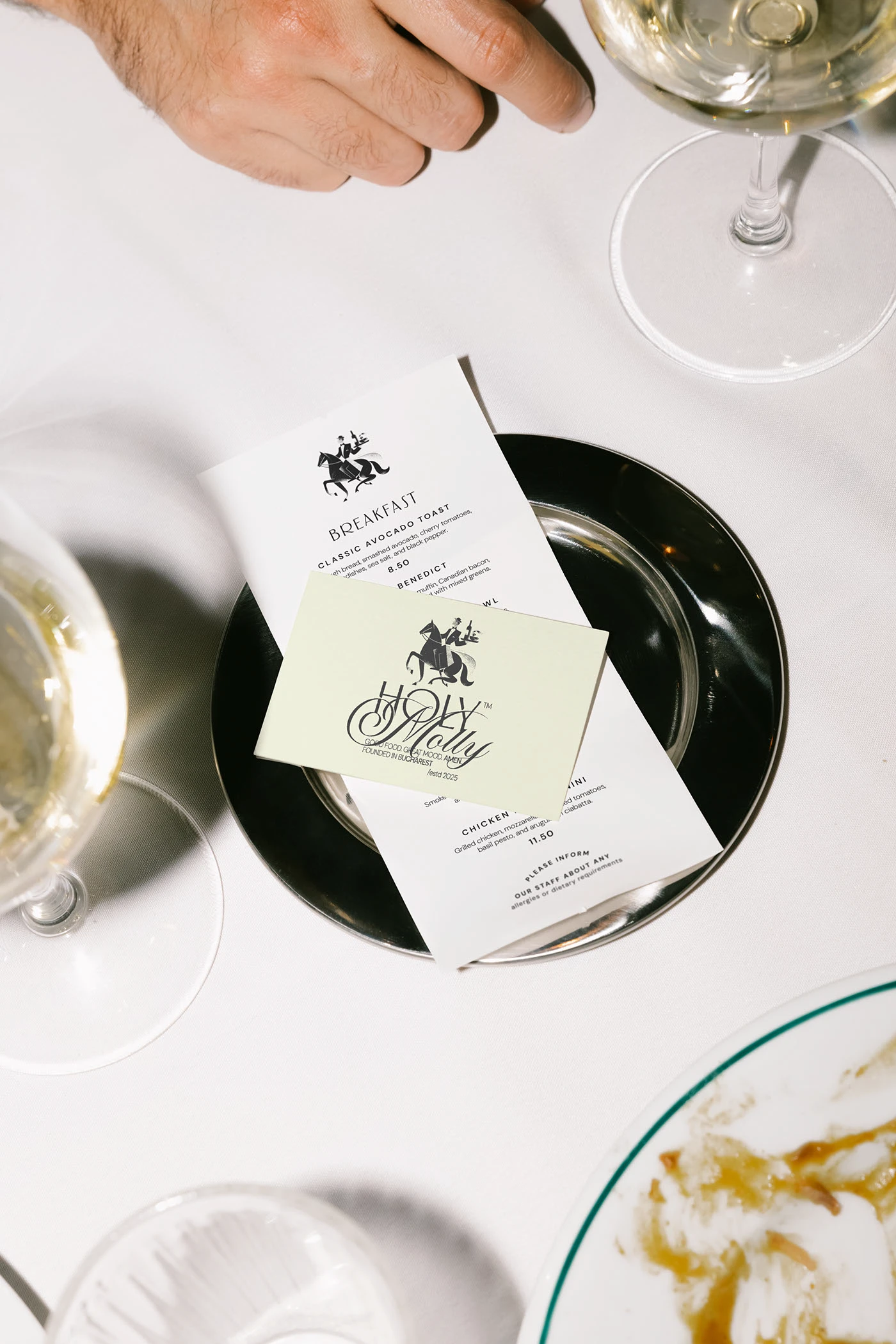 Holy Molly menu card on cream stock laid on a black plate with wine glass — restaurant brand identity