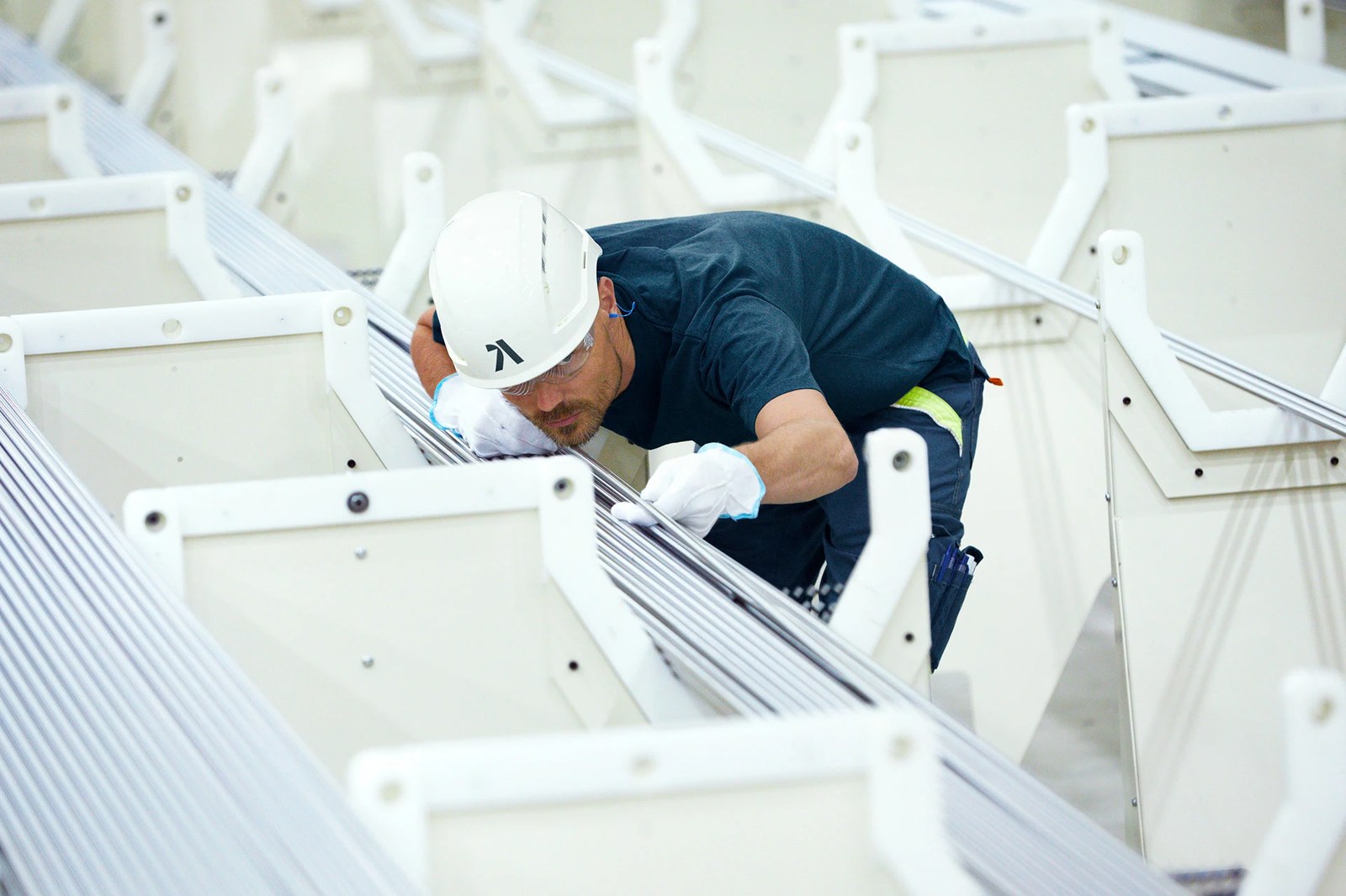 Alleima engineer wearing a white safety helmet stamped with the brand monogram while inspecting stainless steel tubes