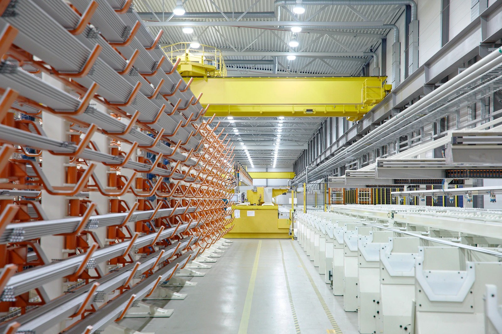 Inside an Alleima manufacturing hall with orange-tipped tube racks and yellow overhead gantry cranes