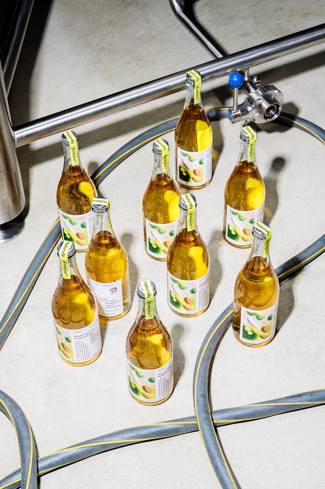 Cluster of condensation-beaded Ambijus Act Naturally bottles on a concrete brewery floor — packaging design by OlssønBarbieri