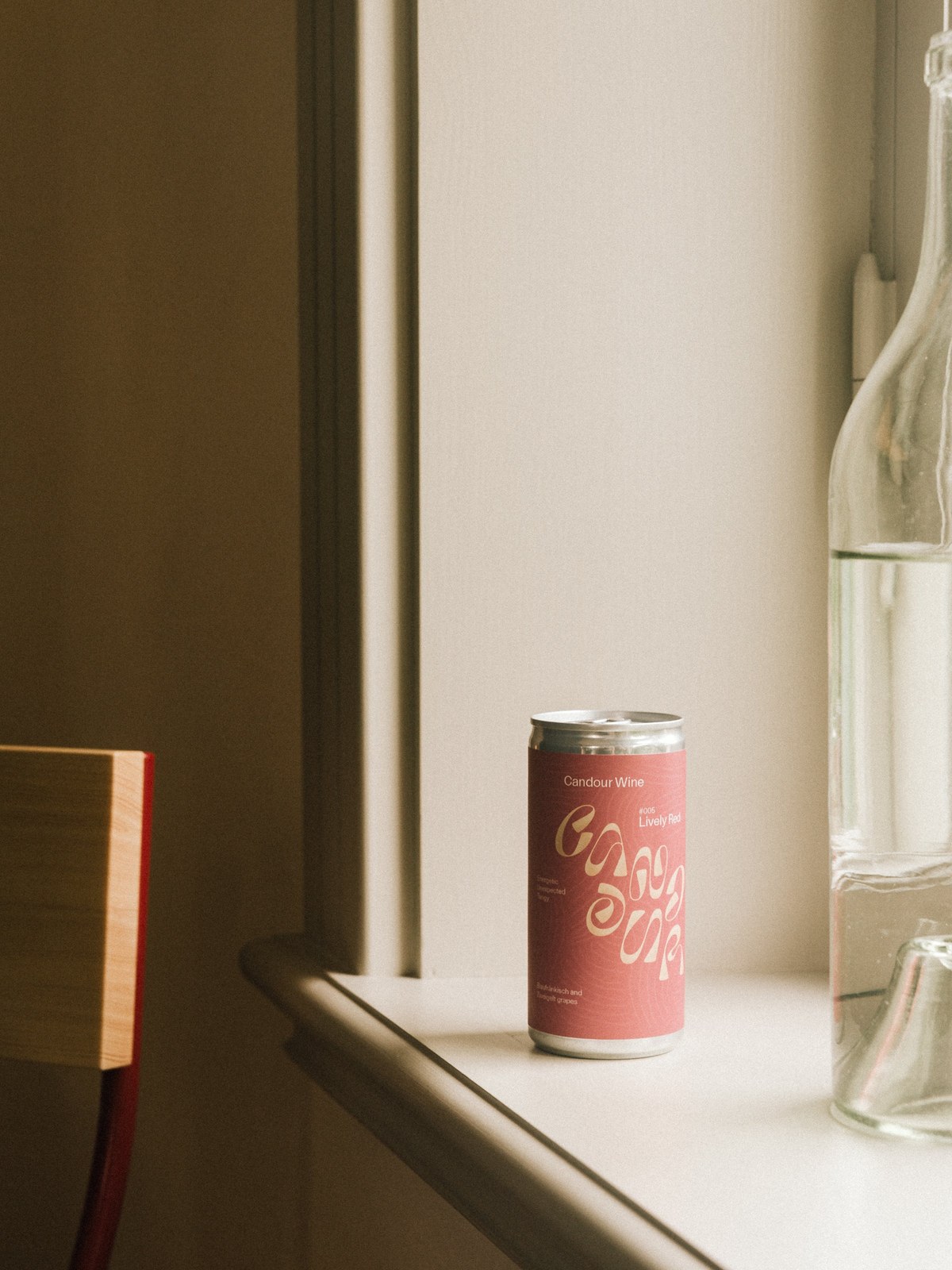 Candour Wine #005 Lively Red can resting on a sunlit window ledge beside a glass bottle