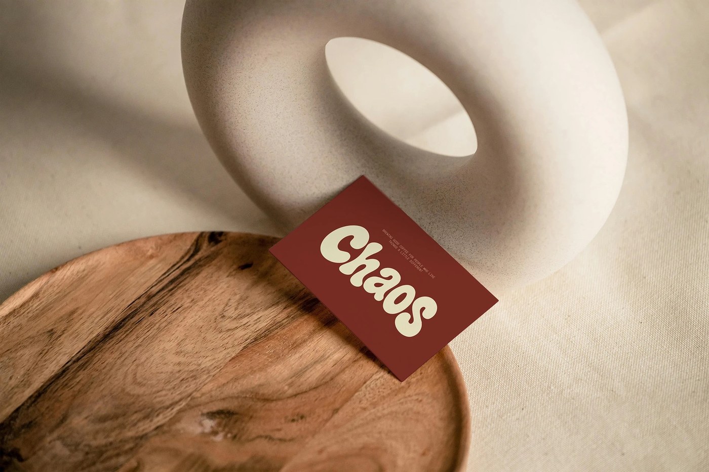 Tactile cream Chaos business card displaying the chubby wordmark balanced between a white ceramic donut sculpture and turned wood tray