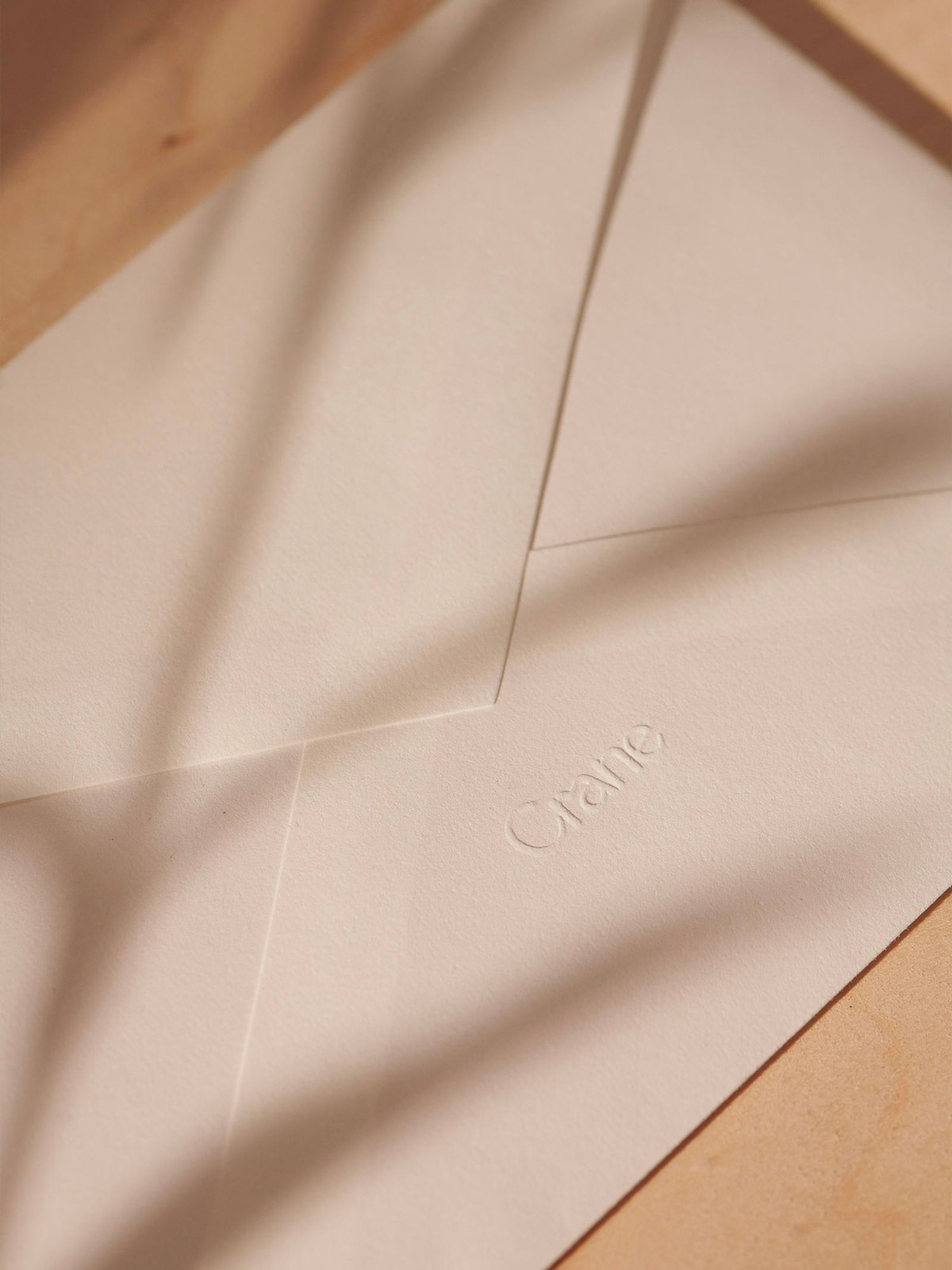 Close-up of blind-debossed Crane logotype on heavy cotton envelope flap in warm sunlight