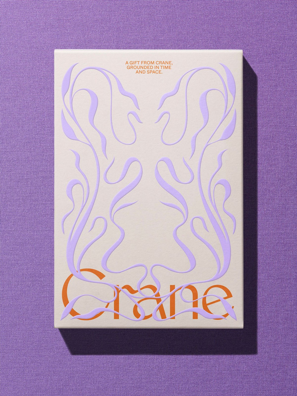 Crane gift box on violet linen with lilac relief flourishes overlapping the orange serif logotype