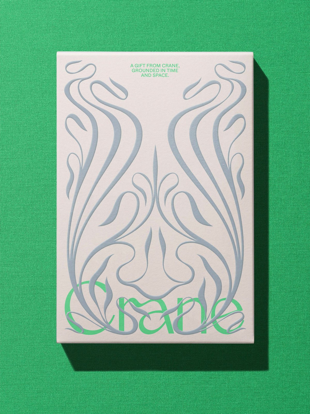 Crane gift box on emerald green cloth with slate-blue embossed botanical scrollwork and green wordmark
