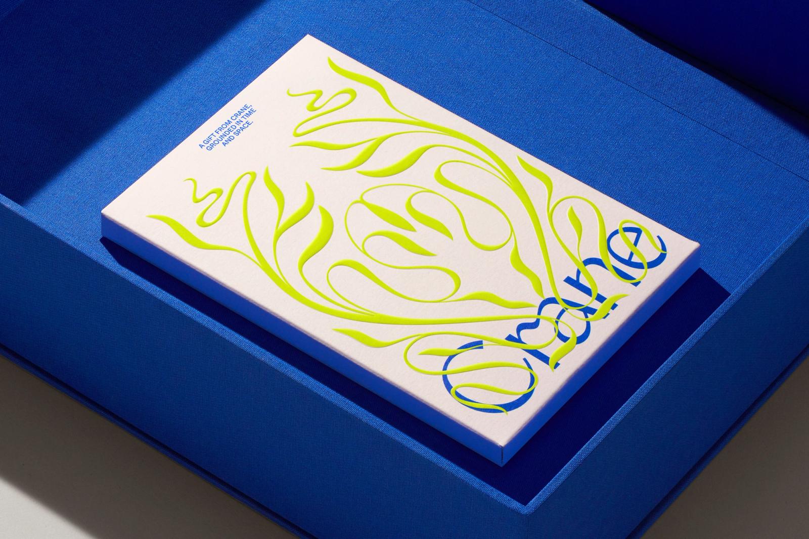 Ecru cotton Crane stationery sleeve with raised neon chartreuse scrollwork inside a cobalt blue tray