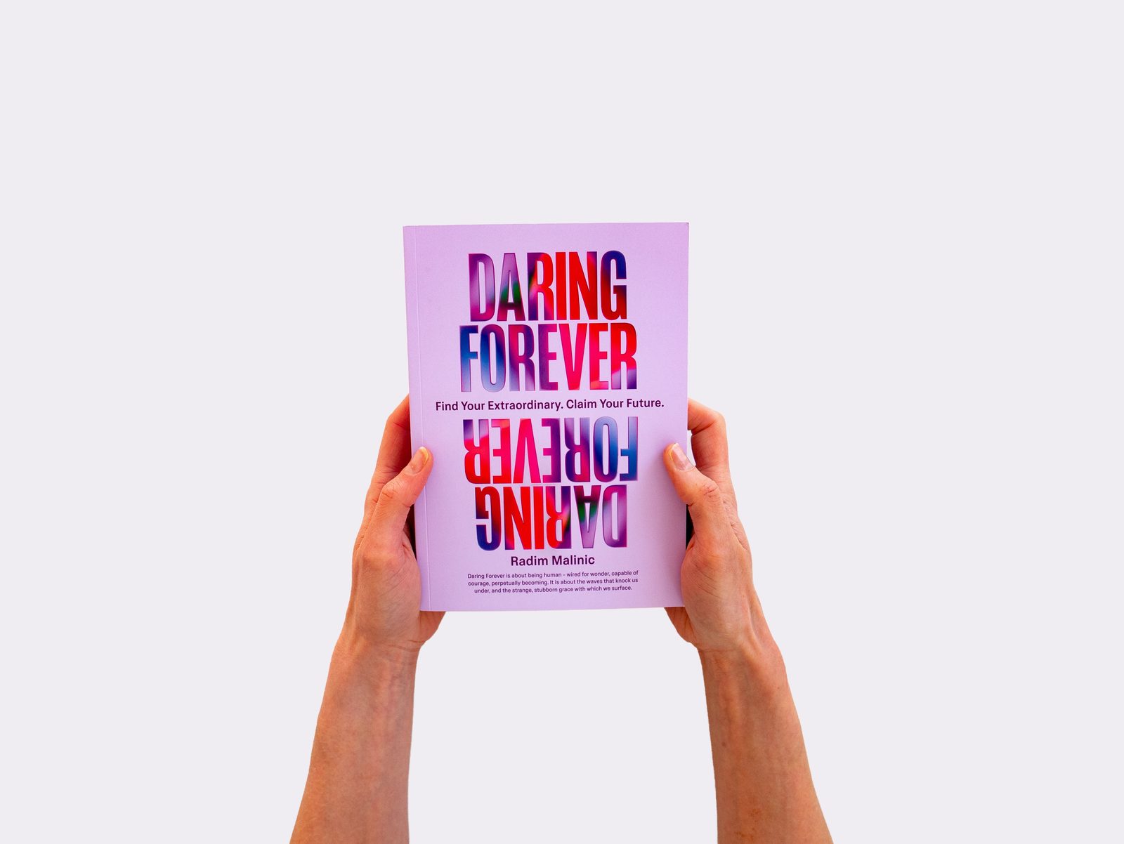 Hands holding up the front cover with mirrored gradient title typography, Daring Forever book by Radim Malinic