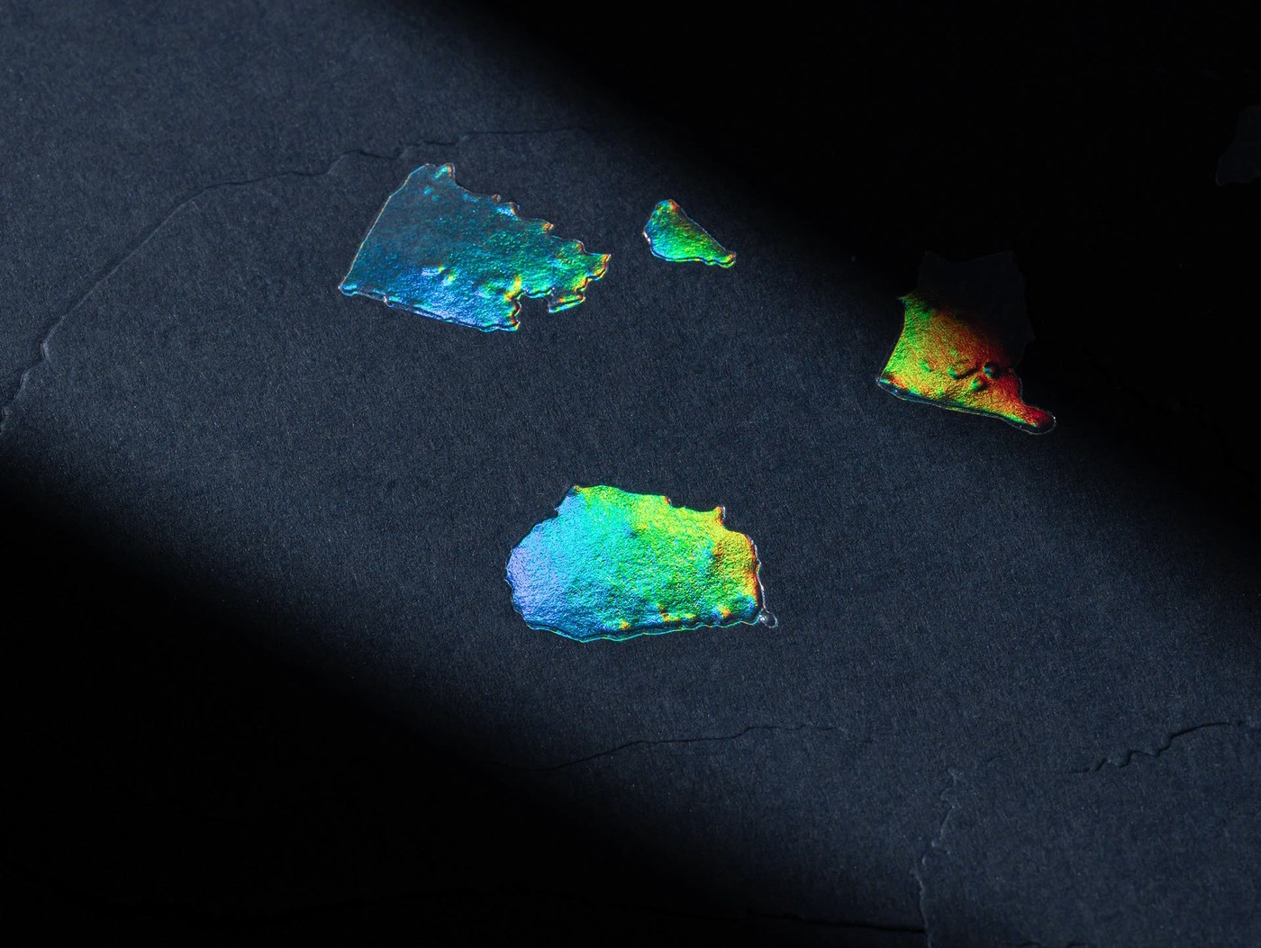 Macro detail of iridescent prismatic foil mineral contours debossed on black paper — branding by Two Times Elliott