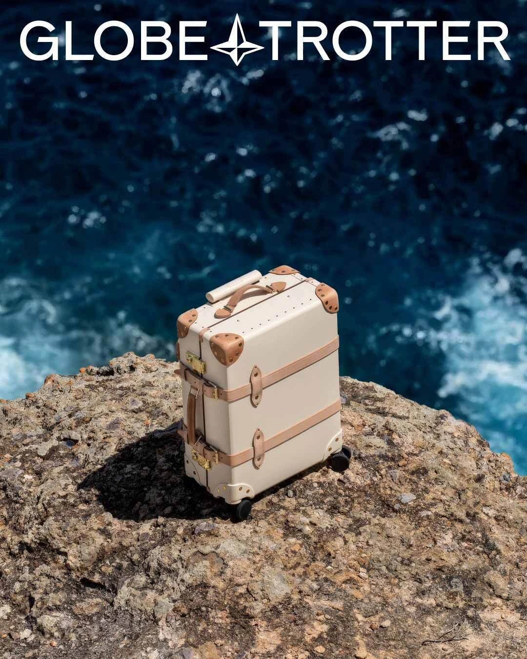 Globe-Trotter campaign layout showing the white uppercase wordmark above an ivory Safari suitcase on coastal rock — brand identity by Ragged Edge