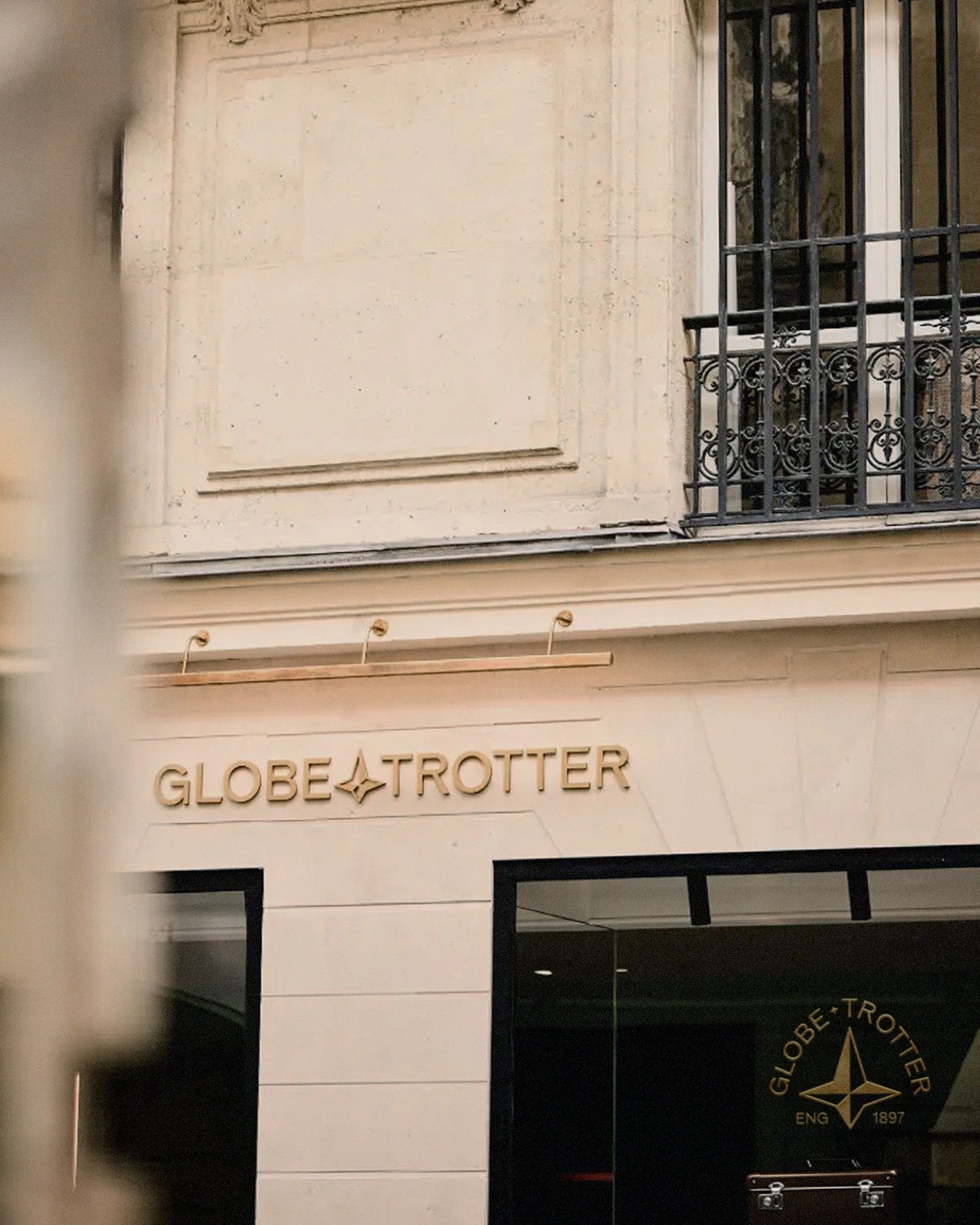 Dimensional brushed-brass Globe-Trotter storefront lettering with the beveled North Star compass on the limestone facade — brand identity by Ragged Edge