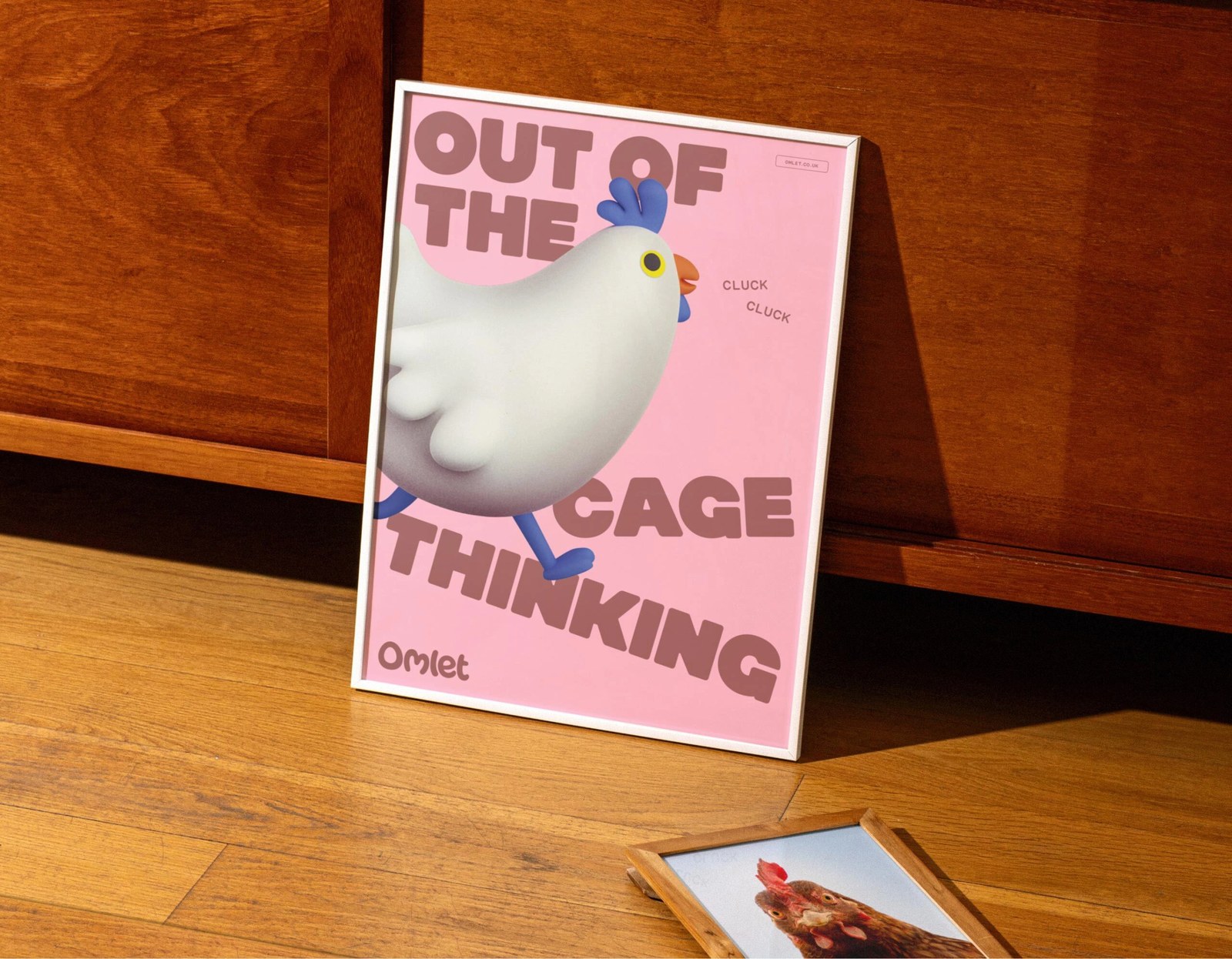 Framed blush-pink Curious Collective chicken poster with angled Out of the Cage Thinking typography in Omlet brand identity by Ragged Edge