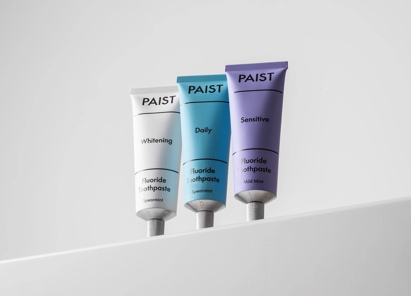 Paist recyclable aluminum toothpaste tube trio in white, sky blue, and lilac on architectural ledge