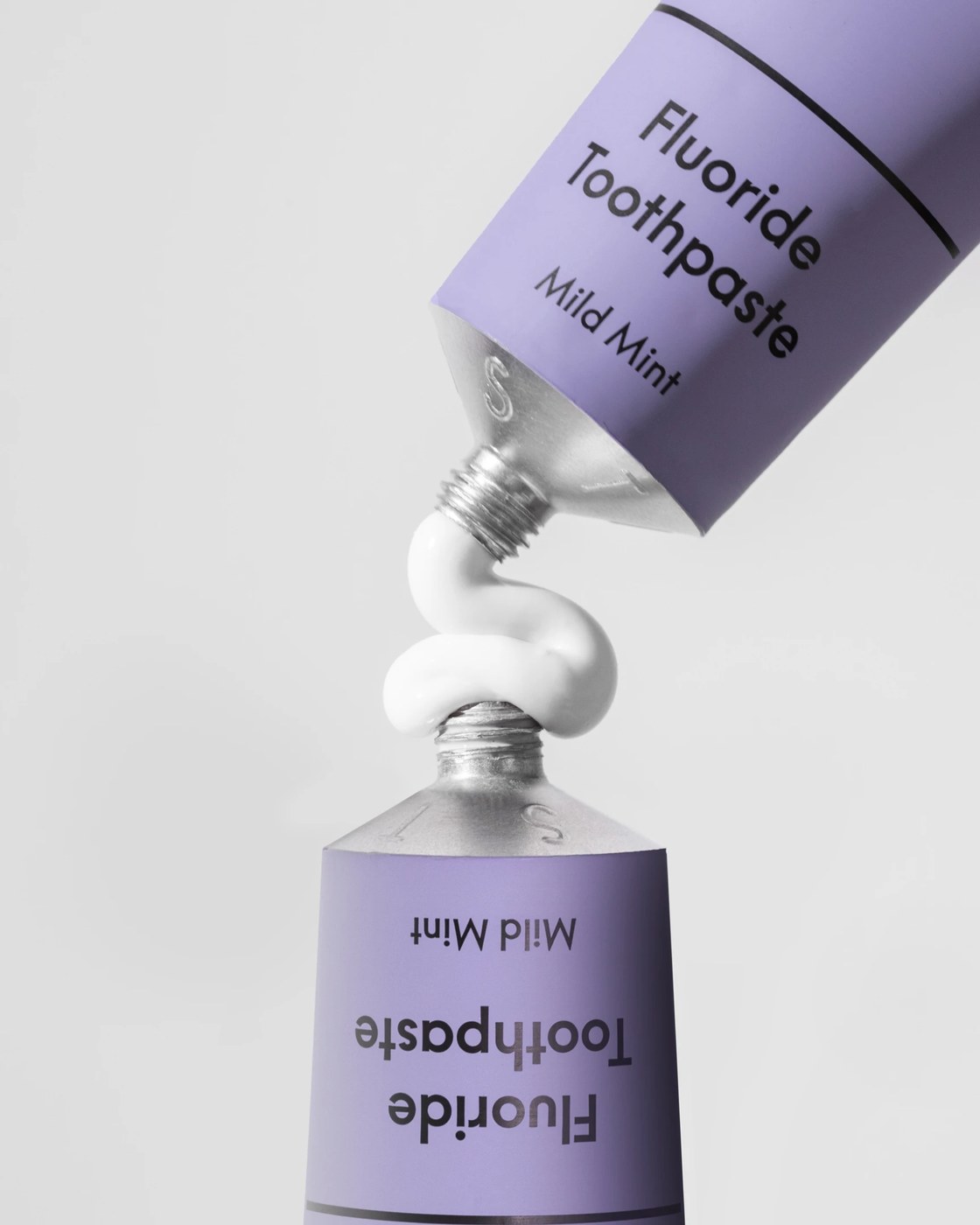 Macro detail of Paist aluminum toothpaste tubes connected by a sculptural ribbon of paste