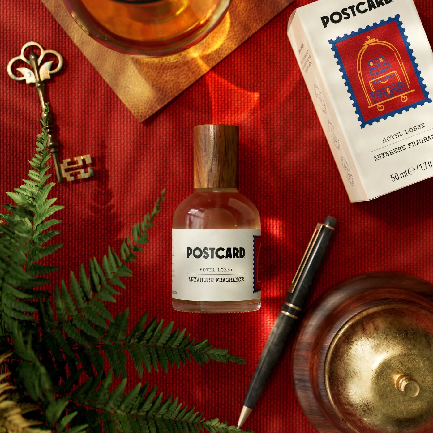Postcard Hotel Lobby Anywhere Fragrance bottle and bellhop luggage stamp box on red fabric — packaging design by Robot Food