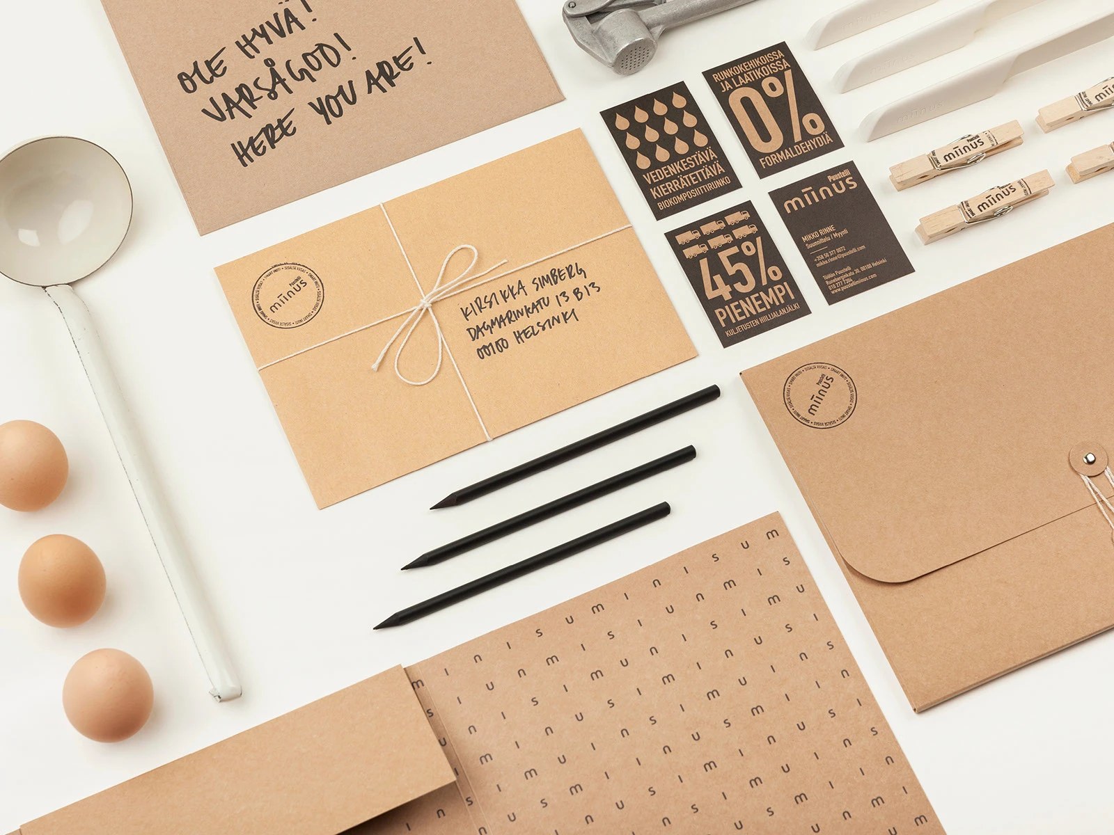 Puustelli Miinus brand identity stationery flat lay with kraft envelopes, charcoal infographic cards, and biocomposite knives by BOND Creative Agency