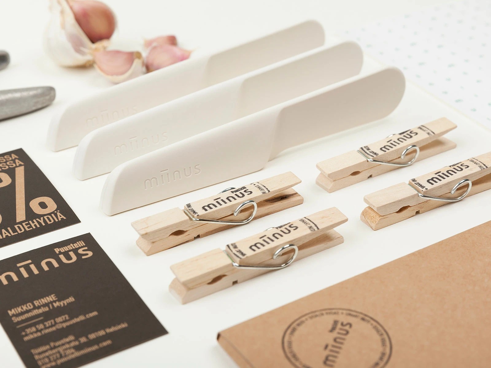 Molded white biocomposite butter spreaders debossed with the miinus logo alongside branded wooden clothespins and business cards