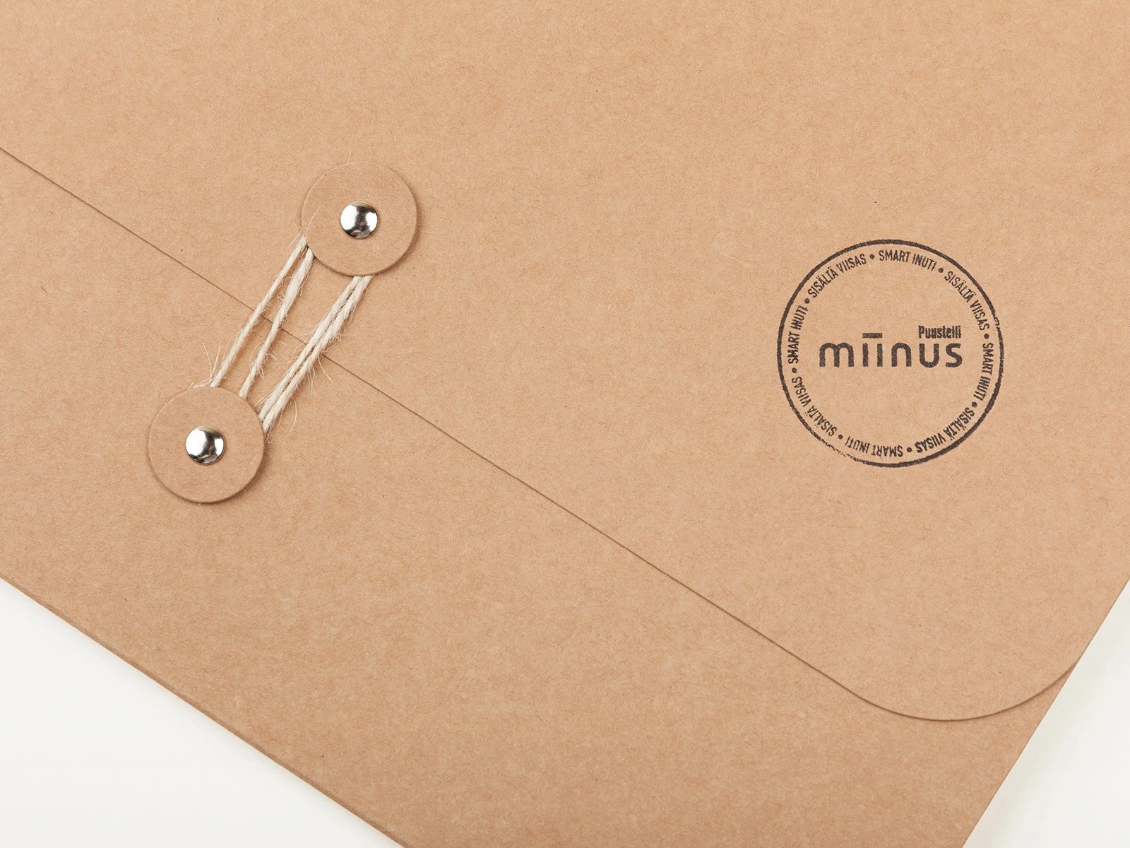 Close-up of raw kraft string-and-washer folder stamped with the circular Puustelli Miinus seal by BOND Creative Agency