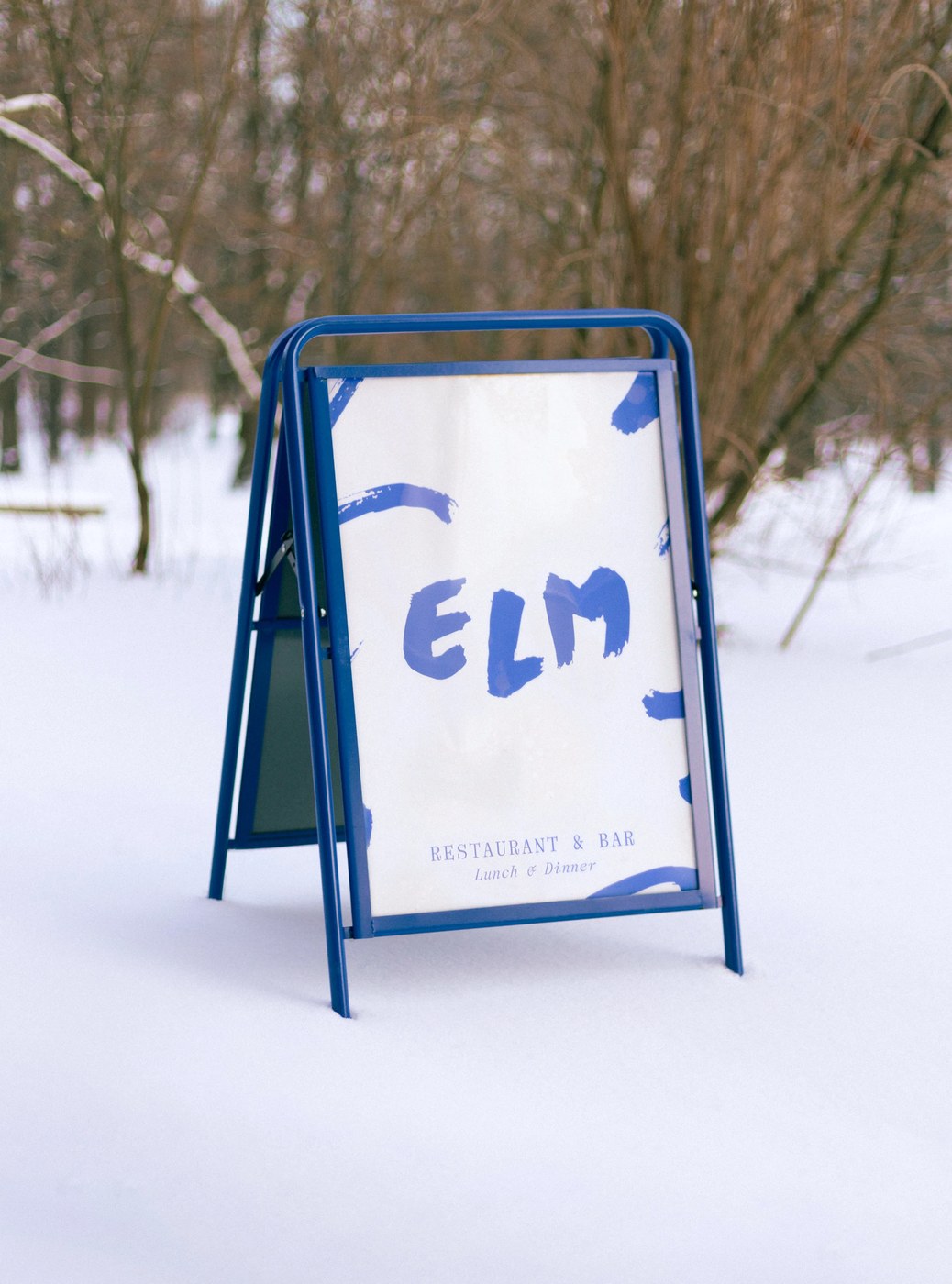 Outdoor blue steel A-frame sidewalk sandwich board sign in the snow with Elm logo