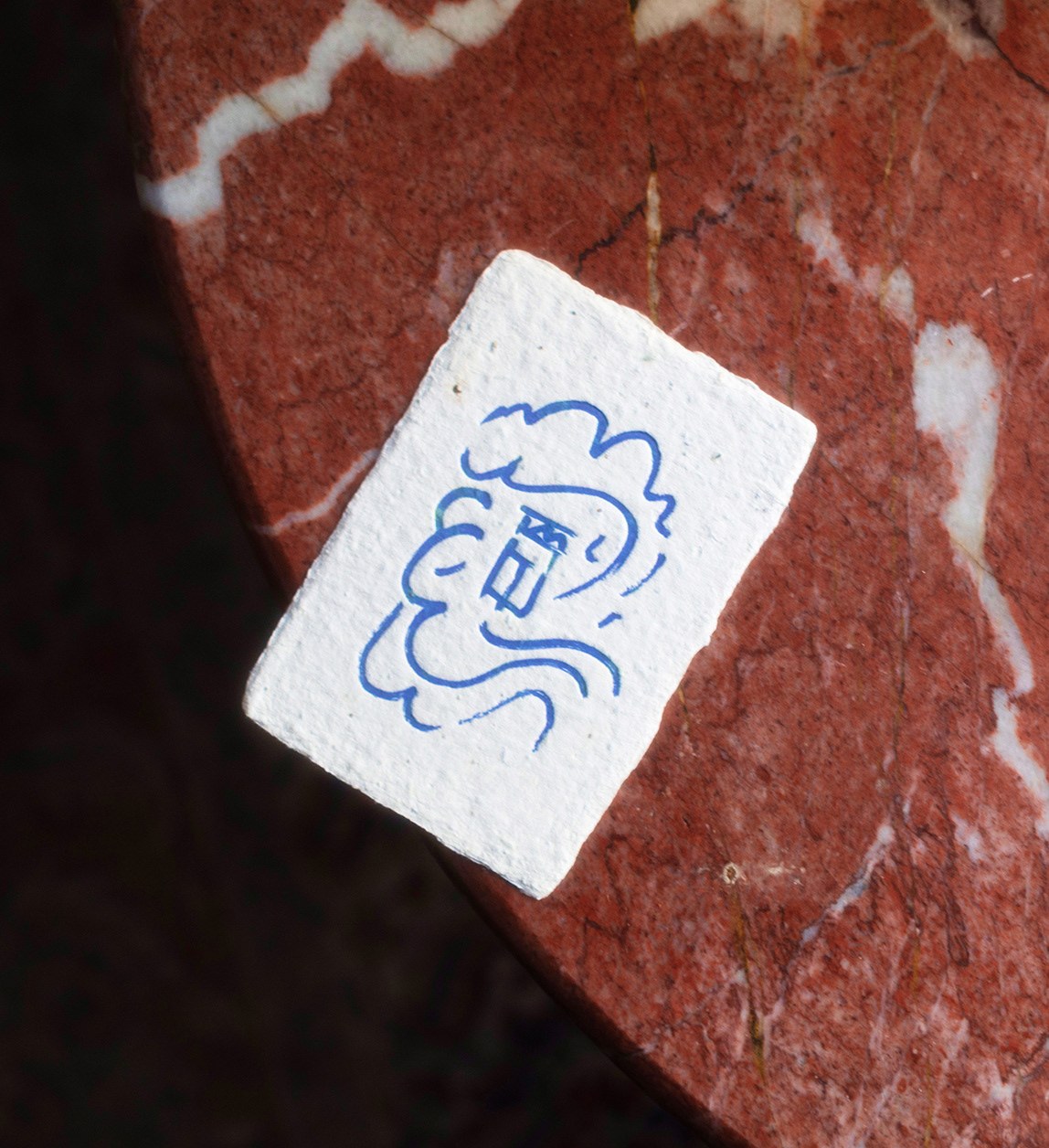 Close-up of handmade deckle-edge card stamped with blue Elm logo on red marble