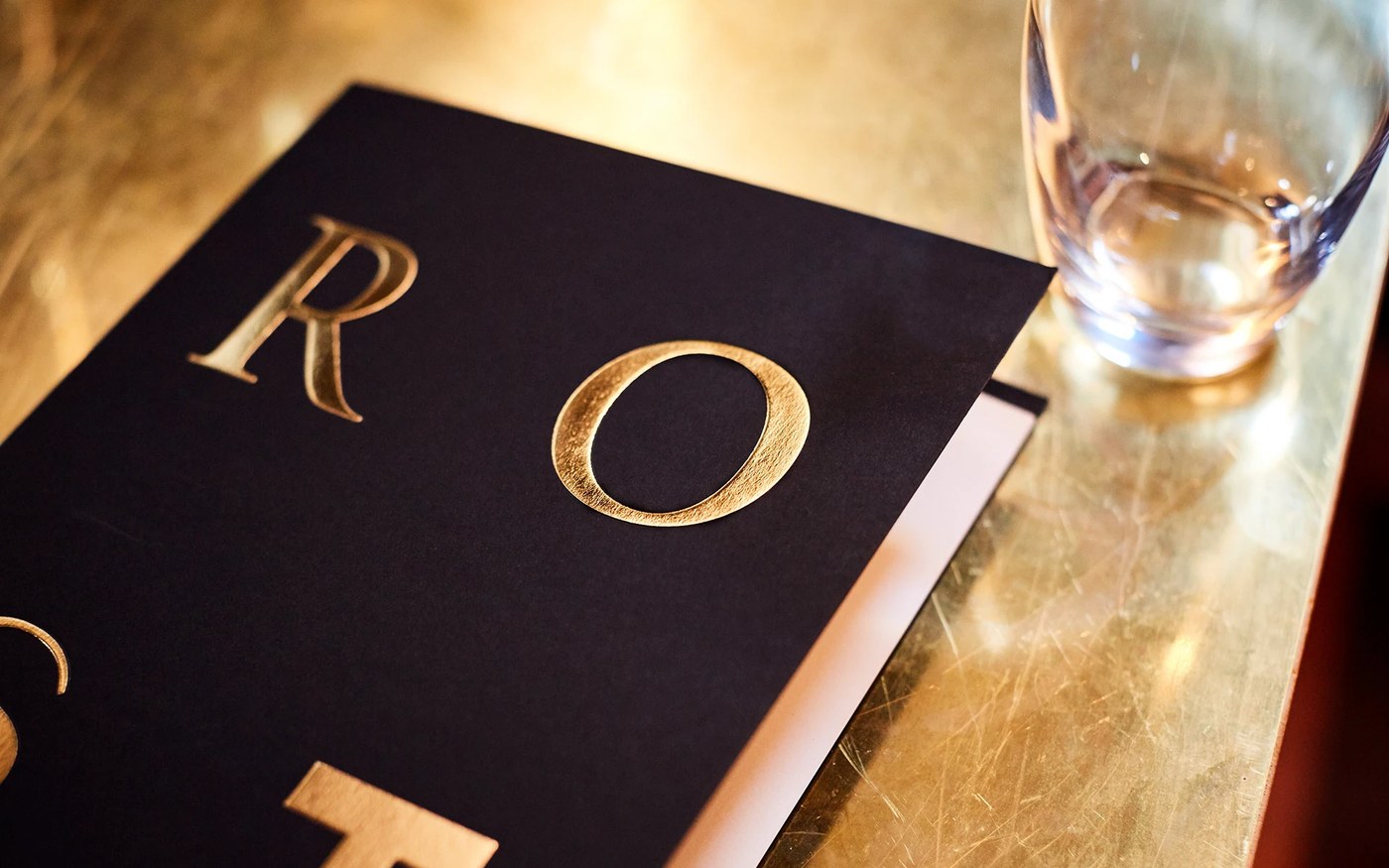 Macro detail of metallic gold foil stamped lettering on matte black paper menu card in Roster branding design by BOND
