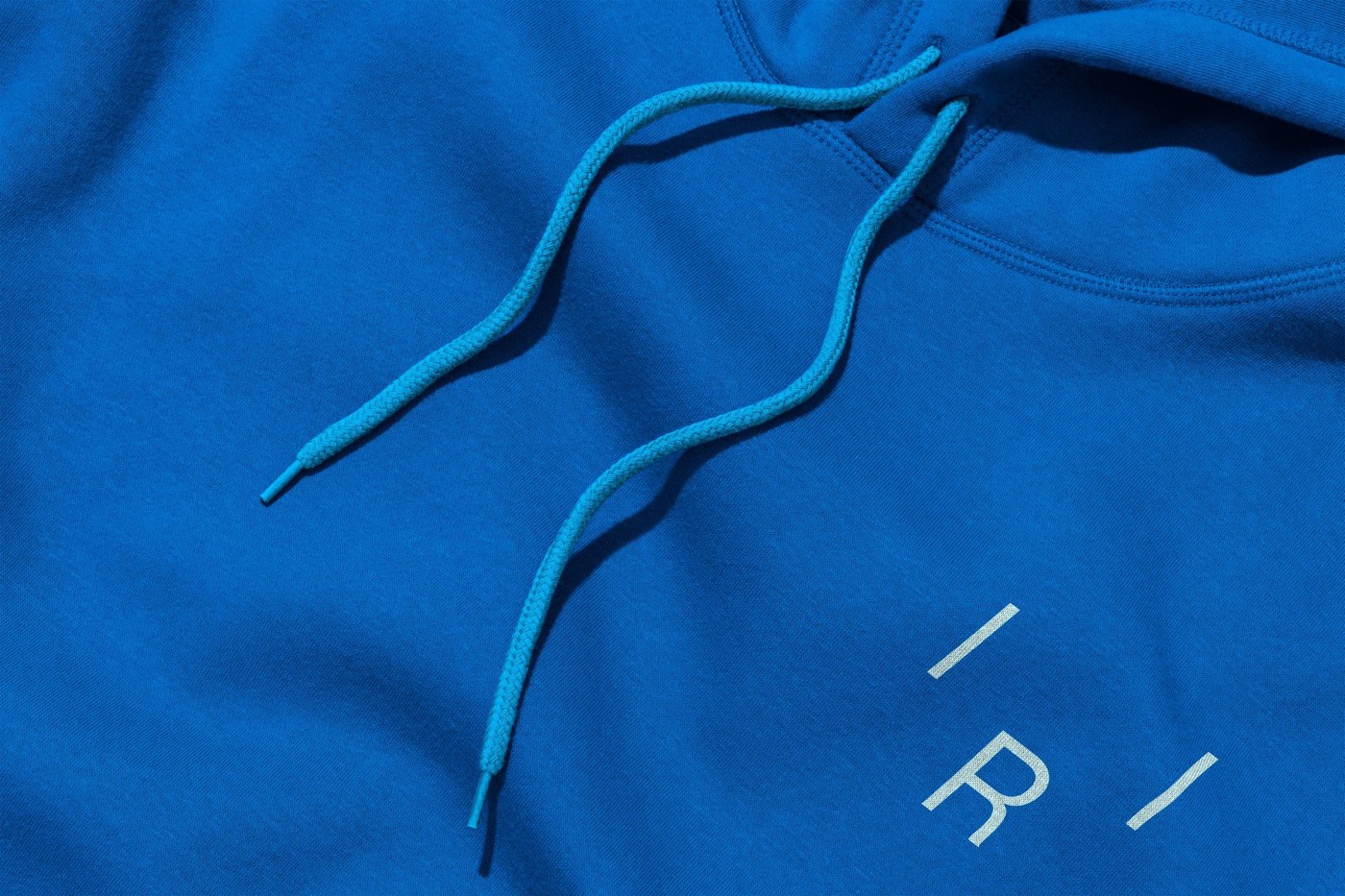 Macro detail of heavy cobalt blue cotton hoodie with white satin-stitch embroidered R calibration monogram