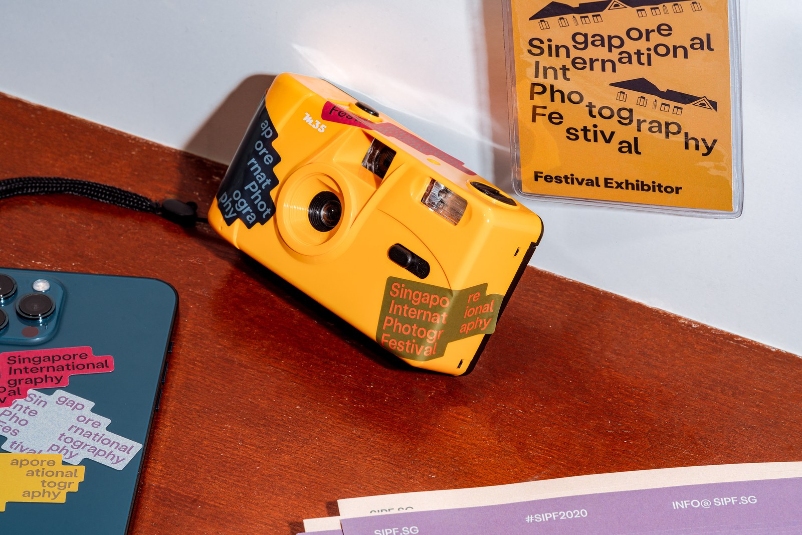 Close-up of yellow 35mm film camera and smartphone wrapped in stepped die-cut SIPF stickers on a wooden desk