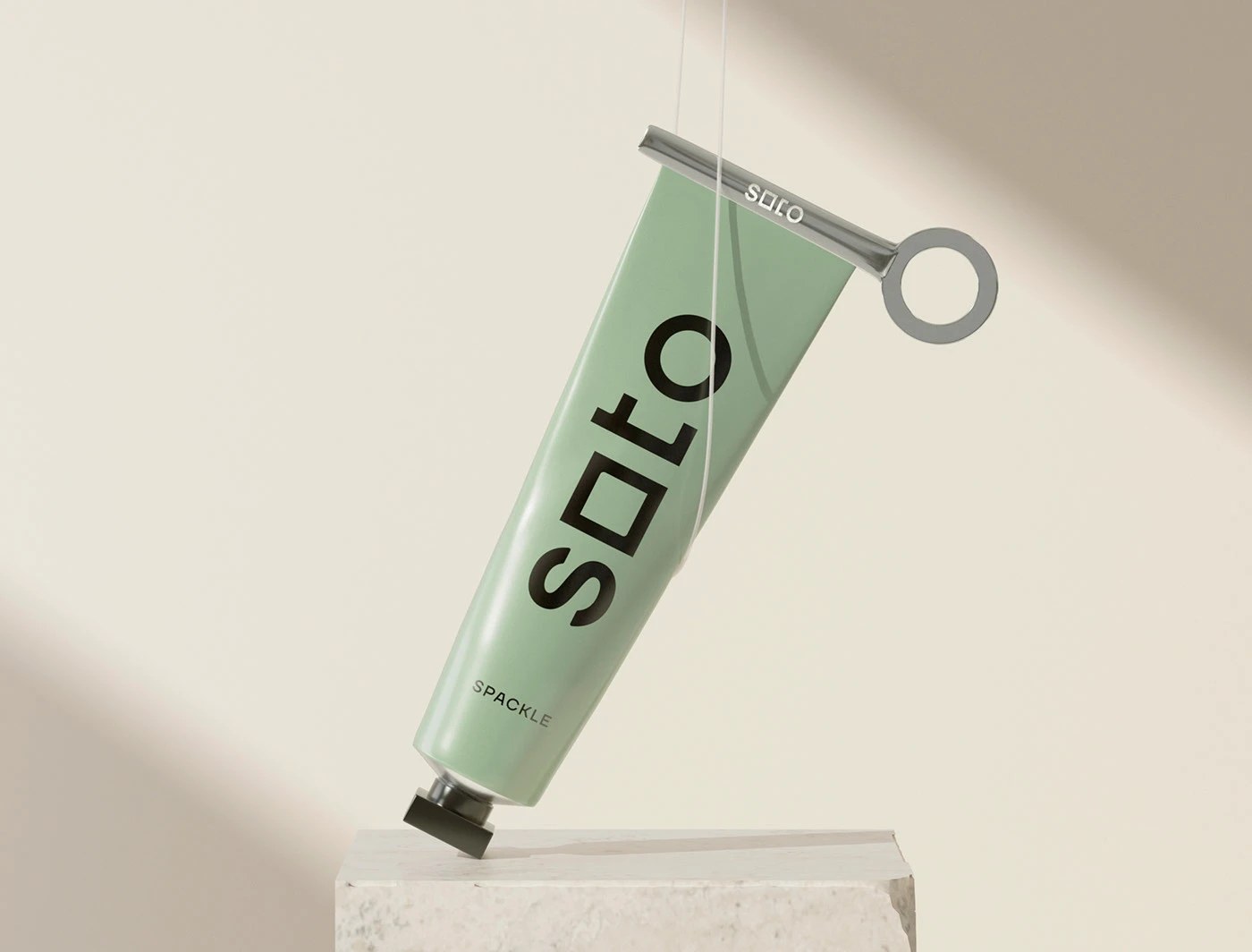 Soto branding sage green spackle tube with wordmark at 200pt beside a chrome key-winder tool on white marble