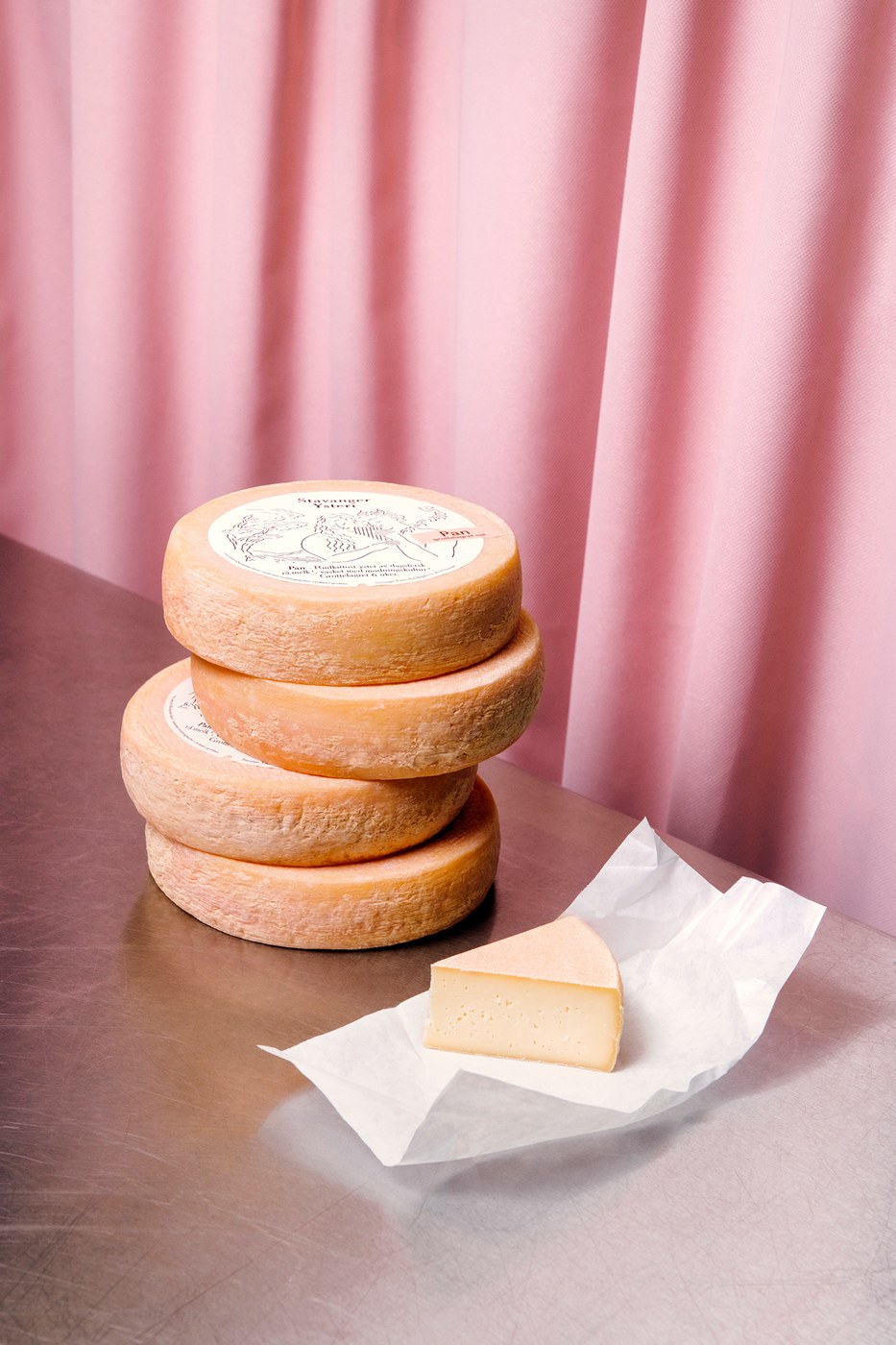 Stack of Pan cheese wheels beside a cut wedge resting on waxed paper wrap in packaging design by OlssønBarbieri