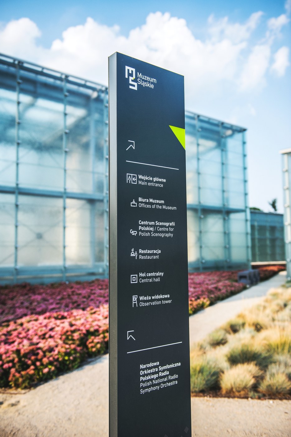 Slender directional totem detail with minimalist iconography and clean typography in museum spatial design