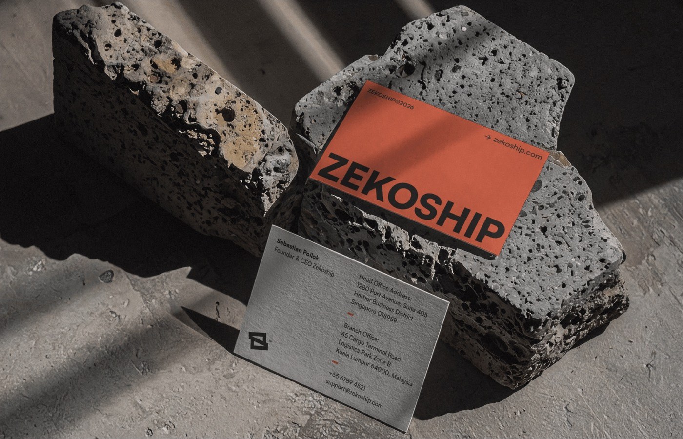 Tactile ZEKOSHIP business cards in vibrant coral and textured cardstock resting on raw concrete stones