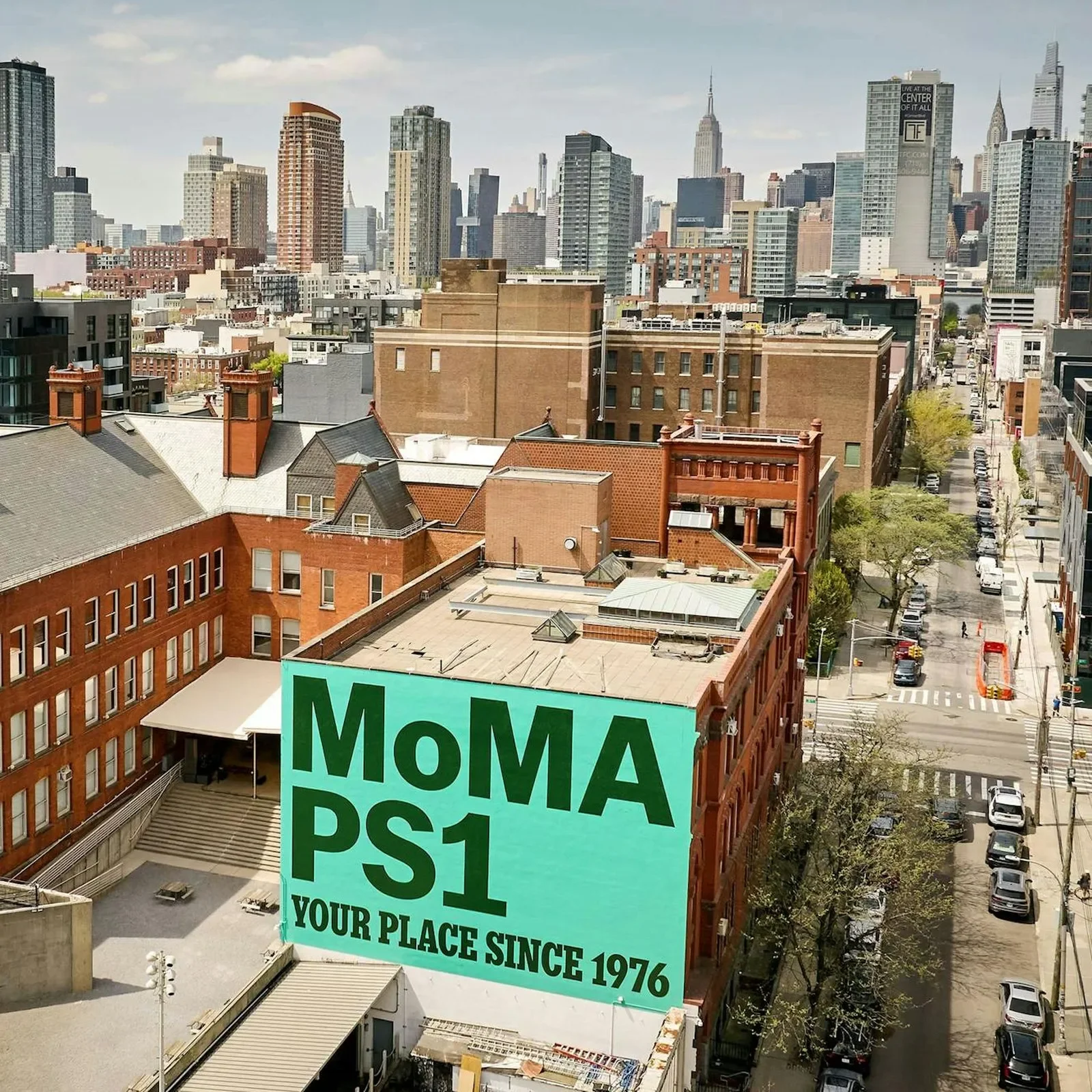 Aerial view of the MoMA PS1 building with the PS1 IS YOUR PLACE anniversary mural painted on the brick facade