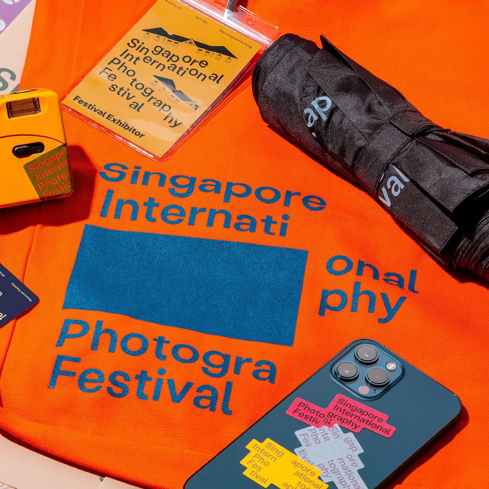 Singapore International Photography Festival graphic design system by Foreign Policy Design with orange tote bag, yellow M35 film camera, passes, and stickers