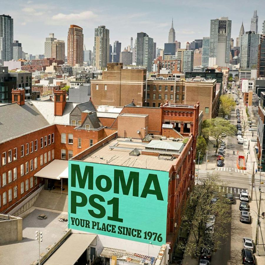 Aerial view of the MoMA PS1 building with the PS1 IS YOUR PLACE anniversary mural painted on the brick facade