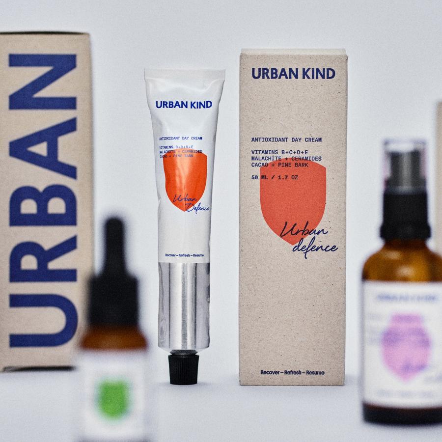 Urban Kind skincare packaging by EVERLAND — kraft carton with giant blue wordmark, aluminium tube with orange shield, shield cartons