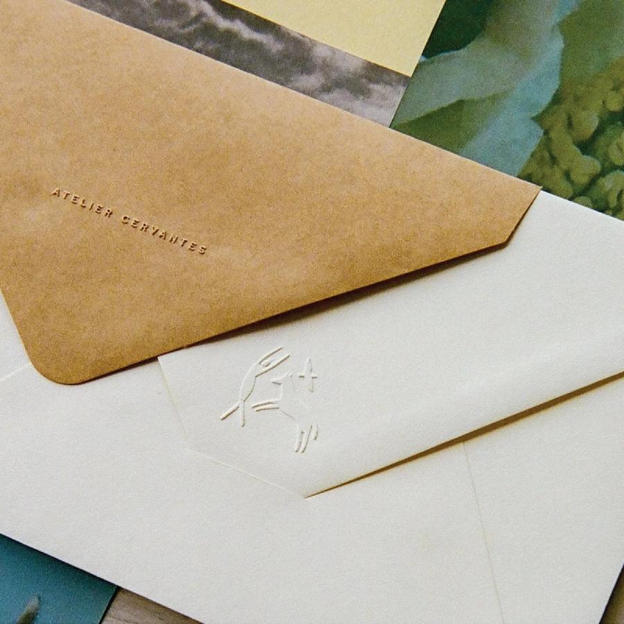 Blind debossed Atelier Cervantes typography and embossed emblem on tactile stationery envelopes by SAVVY STUDIO
