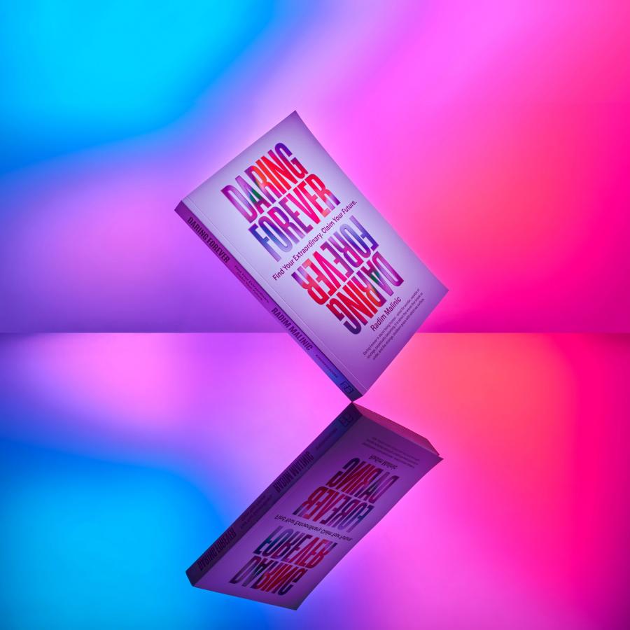 Daring Forever paperback balanced on a mirrored surface against a blue and pink gradient, Daring Forever book by Radim Malinic