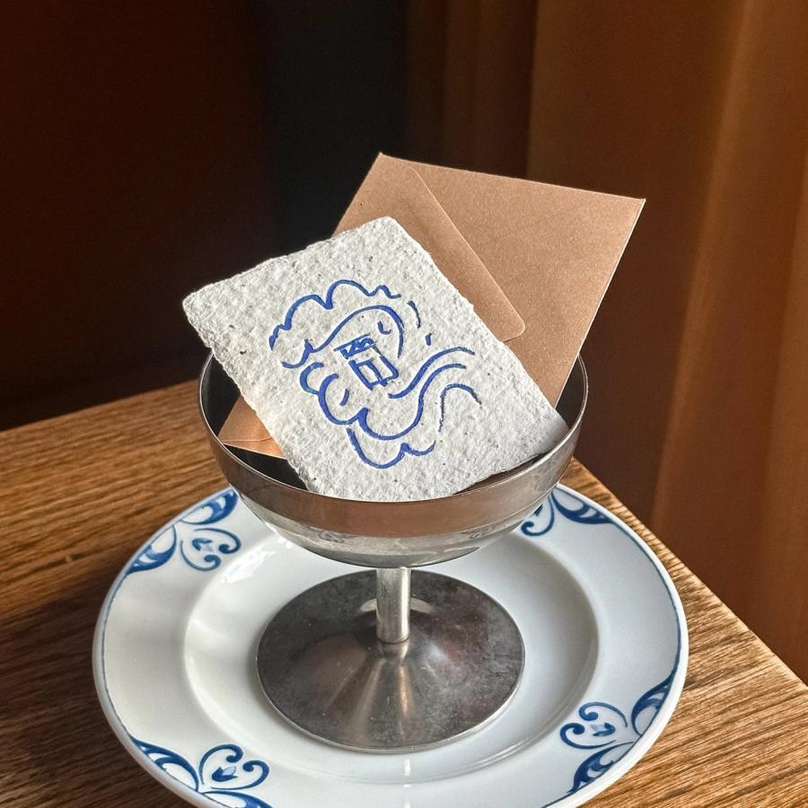 Handmade deckle-edge paper card stamped with blue Elm logo inside a silver coupe